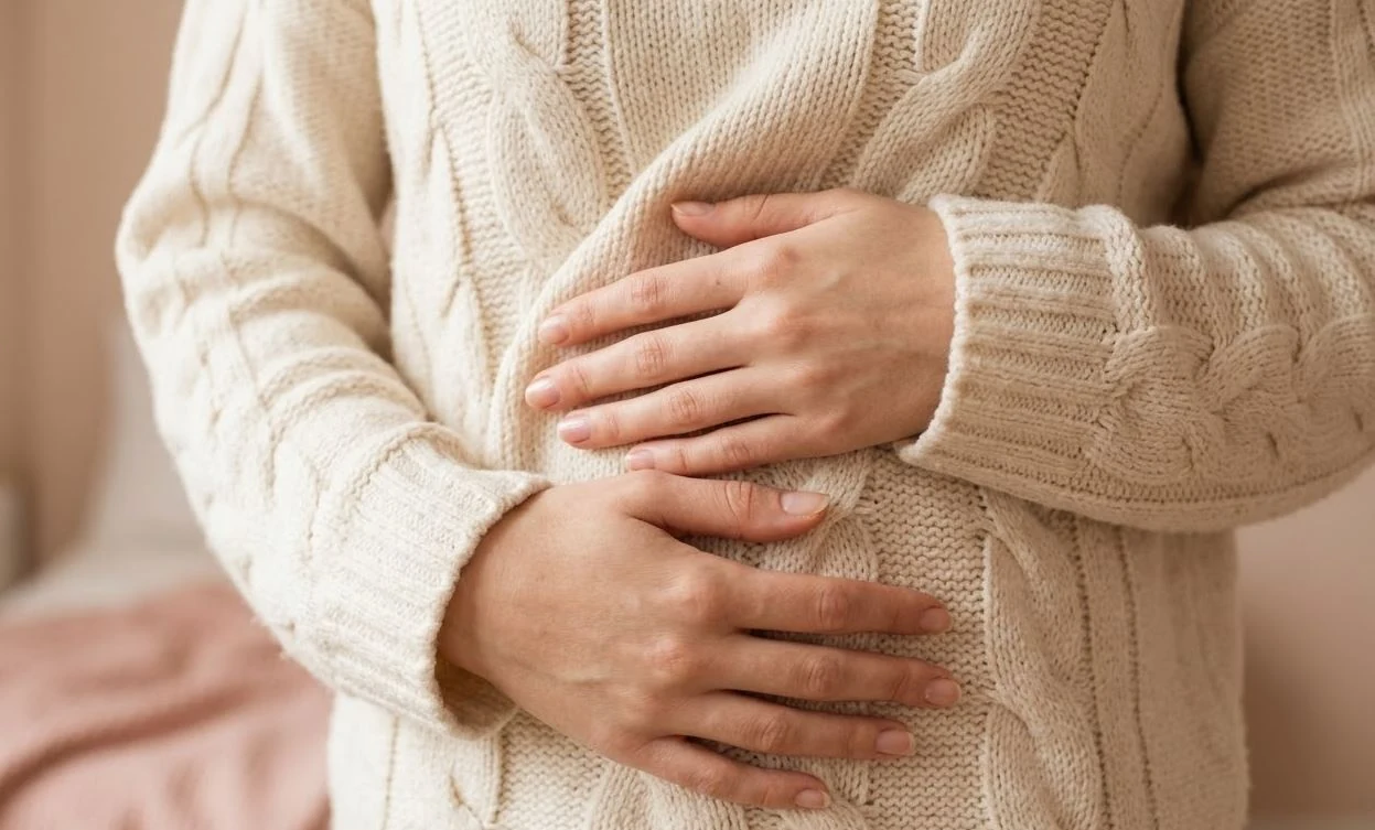 Manos apoyadas sobre el abdomen, sobre un suéter de lana claro